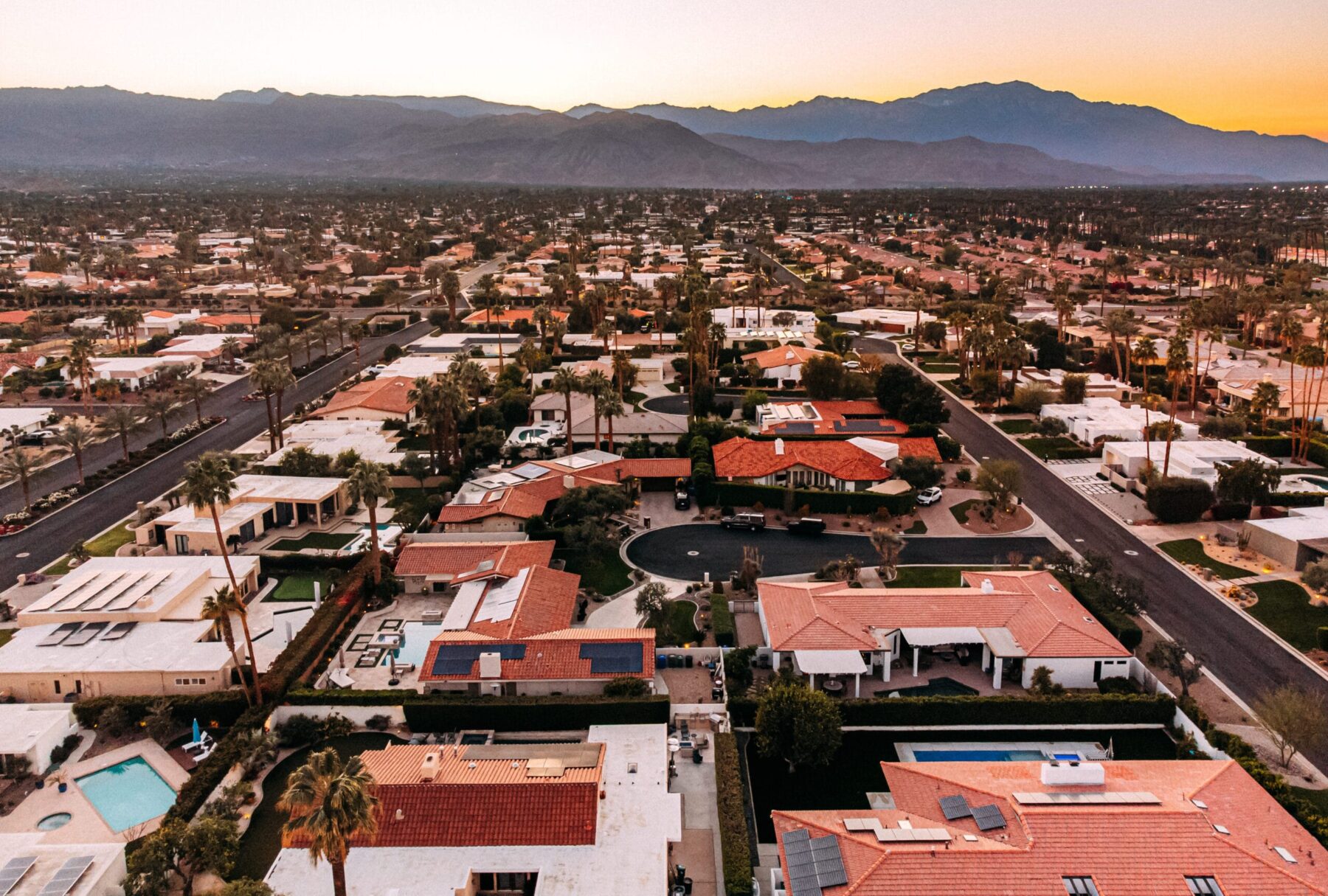 Aerial view of residential neighborhoods in Palm Desert, California at sunset, with palm trees and mountain ranges in the background.