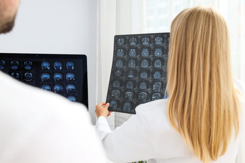 Two doctors examine MRI images of a human brain in a medical office.