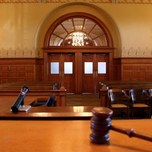 A wooden courtroom interior with empty seats and a gavel on the judge's bench.