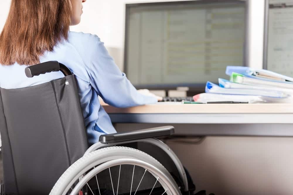 Disabled woman sitting wheelchair working office desk computer