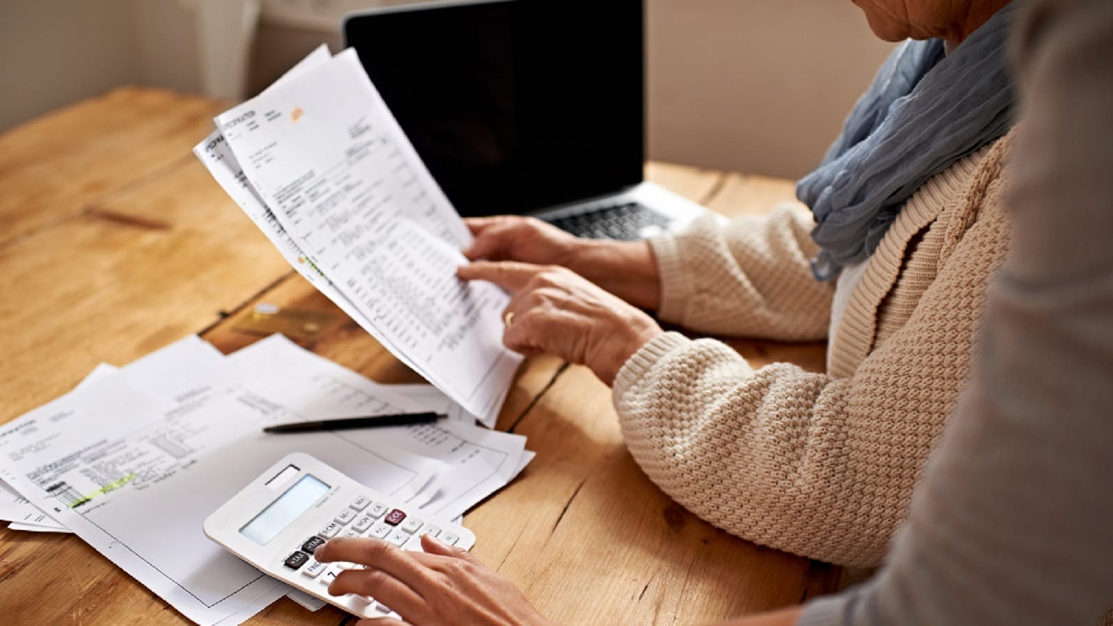 Two people reviewing financial documents at a desk with a calculator and laptop.