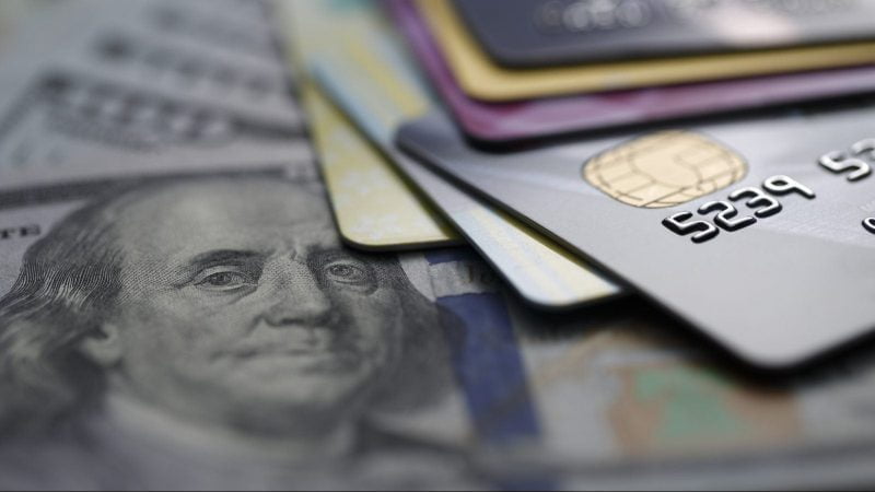 A close-up image of several credit cards stacked on top of U.S. hundred-dollar bills.