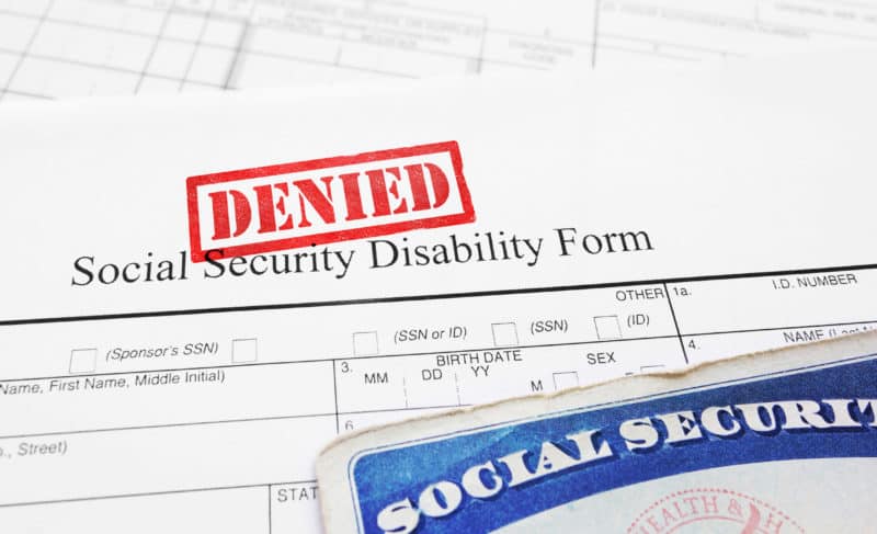 A Social Security card sits atop a denied Social Security Disability Form.