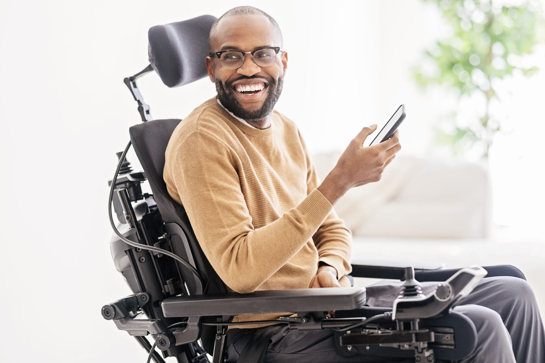 A man in a wheelchair is smiling and using his phone.