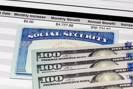 Three $100 bills on top of a social security card and benefit amount spreadsheet
