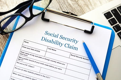A Social Security Disability claim form with a pen and a pair of glasses lying on top of it.
